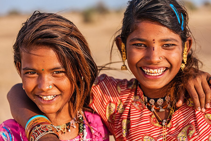 Two young girls with their arms around each other smiling.